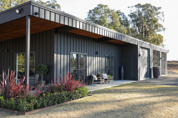 A Fair Dinkum Builds Shed featuring SharpLine cladding with an outdoor patio area wrapped by a neat garden